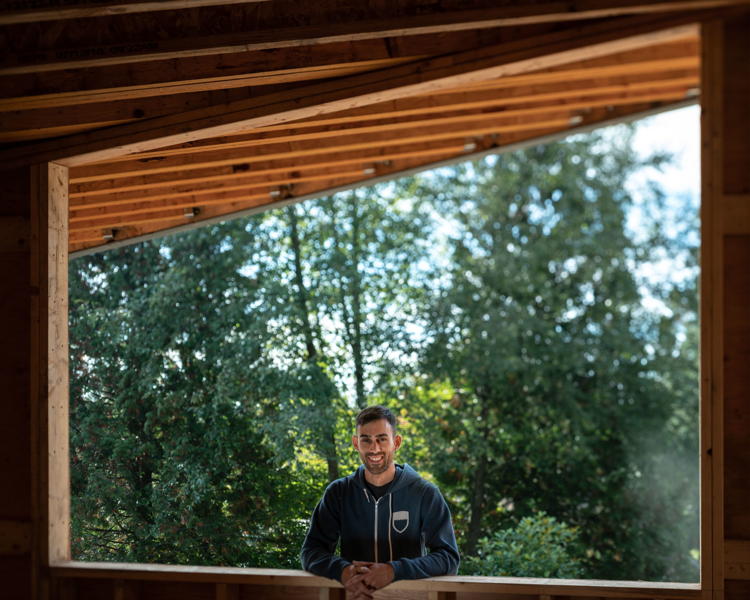 A carpenter stands in a framed-inn picture window with trees behind him.